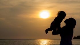 Silhouette Of Female Holding Little Girl At Sunset Sun Reflection In Sea Surface