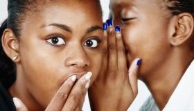 It's a scandal! Beautiful young woman whispers gossip to her friend, who looks shocked