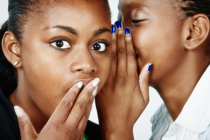 It's a scandal! Beautiful young woman whispers gossip to her friend, who looks shocked