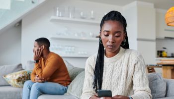 Shot of a young woman ignoring her partner while using a cellphone at home