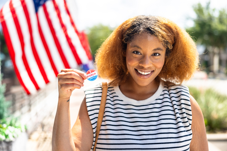 Portrait of a beautiful black woman in front of an American Flag with I Voted sticker