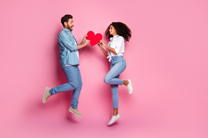 Joyful couple holding heart-shaped symbol against pink background, symbolizing love and relationship