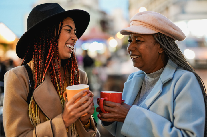 Happy african mother and daughter having fun together at Christmas market drinking hot chocolate - Winter holiday, travel and family lifestyle